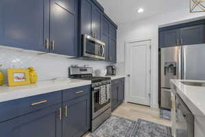 Kitchen with blue cabinetry, stainless steel appliances, decorative backsplash, light stone counters, and recessed lighting