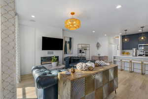 Living area featuring light wood-type flooring, recessed lighting, a chandelier, and a glass covered fireplace