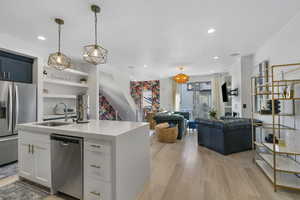 Kitchen with stainless steel appliances, decorative light fixtures, light wood finished floors, backsplash, and open floor plan