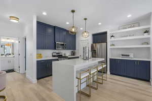 Kitchen featuring blue cabinetry, a breakfast bar, tasteful backsplash, light stone countertops, and stainless steel appliances