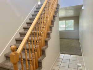 Stairway featuring tile patterned floors, carpet, and a textured ceiling