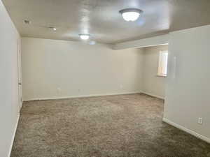 Carpeted empty room with a textured ceiling and baseboards