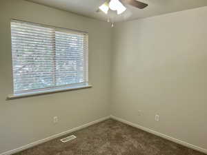 Unfurnished room with dark colored carpet and a ceiling fan