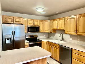 Kitchen with stainless steel appliances, light countertops, light tile patterned floors, a textured ceiling, and backsplash