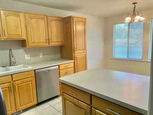 Kitchen featuring stainless steel dishwasher, hanging light fixtures, light tile patterned floors, light countertops, and a chandelier