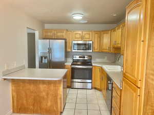 Kitchen with stainless steel appliances, light tile patterned floors, a peninsula, and light countertops