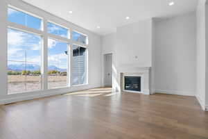 Unfurnished living room featuring a mountain view, recessed lighting, light wood-type flooring, a glass covered fireplace, and a high ceiling