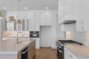 Kitchen featuring glass insert cabinets, stainless steel gas range oven, white cabinets, decorative light fixtures, and recessed lighting