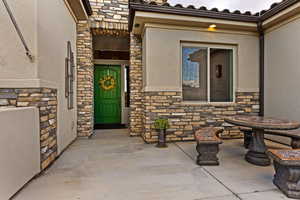 Property entrance featuring stone siding, stucco siding, a patio, and a tiled roof