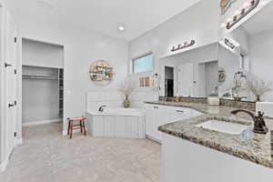 Full bath featuring two vanities, a bath, light tile patterned flooring, a spacious closet, and tiled shower