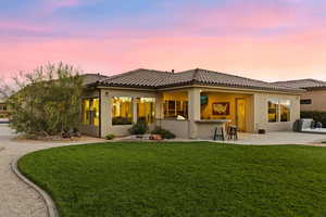Back of property at dusk featuring a yard, stucco siding, a patio, and a tile roof