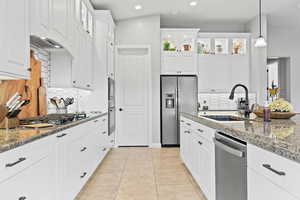 Kitchen featuring white cabinetry, backsplash, hanging light fixtures, stainless steel appliances, and glass insert cabinets