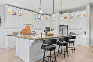 Kitchen with decorative backsplash, glass insert cabinets, a kitchen bar, white cabinets, and recessed lighting