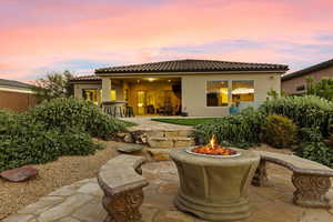 Back of property at dusk featuring a patio area, a fire pit, stucco siding, and a tiled roof