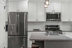 Kitchen with stainless steel appliances, white cabinets, tasteful backsplash, and dark stone countertops