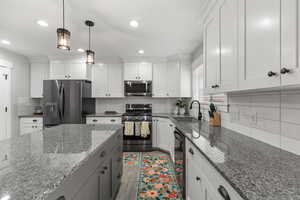 Kitchen with dark stone counters, appliances with stainless steel finishes, decorative light fixtures, tasteful backsplash, and white cabinets