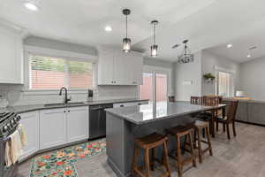 Kitchen with dark stone countertops, a breakfast bar area, stainless steel appliances, white cabinetry, and decorative light fixtures