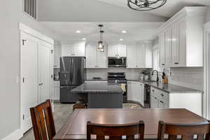 Kitchen featuring decorative light fixtures, dark stone counters, appliances with stainless steel finishes, white cabinetry, and lofted ceiling