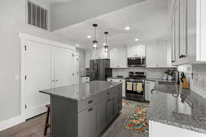 Kitchen featuring dark stone countertops, stainless steel appliances, tasteful backsplash, white cabinetry, and decorative light fixtures
