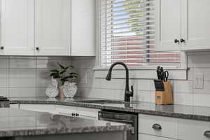 Kitchen featuring white cabinetry, dark stone counters, backsplash, and dishwasher