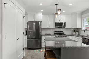Kitchen with appliances with stainless steel finishes, dark stone counters, white cabinets, tasteful backsplash, and recessed lighting