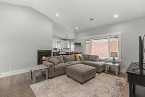 Living area featuring lofted ceiling, recessed lighting, wood finished floors, and a lit fireplace