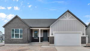 View of front facade featuring brick siding, covered porch, board and batten siding, an attached garage, and driveway