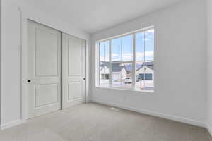 Unfurnished bedroom with light colored carpet, a closet, and a residential view