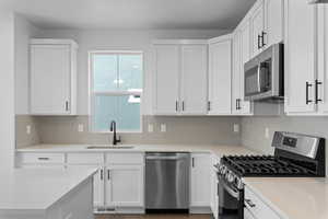 Kitchen with appliances with stainless steel finishes, white cabinets, decorative backsplash, and light stone counters