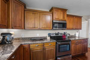 Kitchen with appliances with stainless steel finishes, dark stone countertops, arched walkways, brown cabinetry, and a textured ceiling