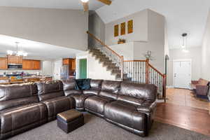 Living room featuring arched walkways, high vaulted ceiling, a chandelier, stairs, and wood finished floors