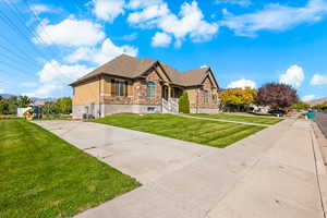 View of front of house with stone siding, a front yard, a porch, stucco siding, and concrete driveway