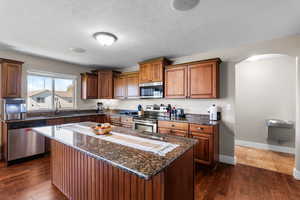 Kitchen featuring dark stone countertops, stainless steel appliances, a center island, a textured ceiling, and brown cabinets