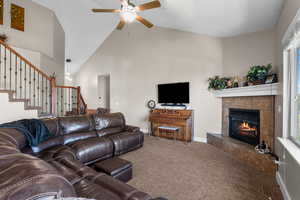 Living room with carpet, a tiled fireplace, high vaulted ceiling, a ceiling fan, and stairway