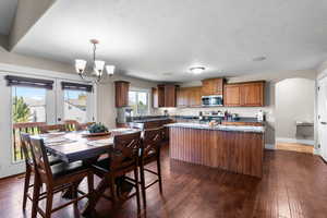 Kitchen featuring arched walkways, dark wood-type flooring, a center island, stainless steel appliances, and a textured ceiling