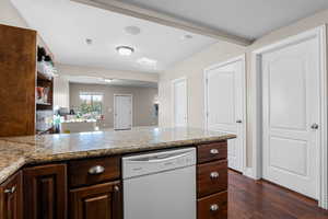 Kitchen featuring dark brown cabinets, white dishwasher, dark wood finished floors, light stone countertops, and beam ceiling