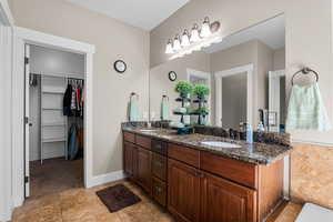 Full bathroom featuring double vanity, a walk in closet, and light tile patterned flooring