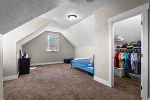 Bedroom featuring a textured ceiling, carpet flooring, a spacious closet, and vaulted ceiling