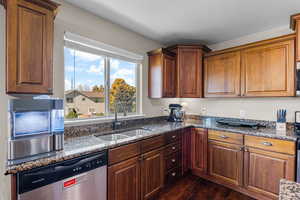 Kitchen featuring dishwasher, dark stone counters, dark wood-style floors, and brown cabinetry