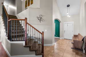 Tiled foyer with high vaulted ceiling, arched walkways, and stairway