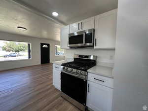 Kitchen featuring stainless steel appliances, a textured ceiling, white cabinetry, dark wood-style floors, and light stone countertops
