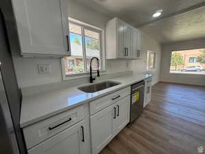 Kitchen featuring light stone countertops, dark wood-style flooring, white cabinetry, dishwasher, and a textured ceiling