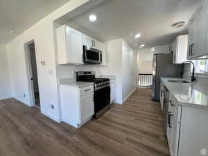 Kitchen featuring appliances with stainless steel finishes, light stone counters, white cabinetry, dark wood-type flooring, and recessed lighting