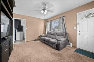 Living room featuring a textured ceiling, light colored carpet, and ceiling fan