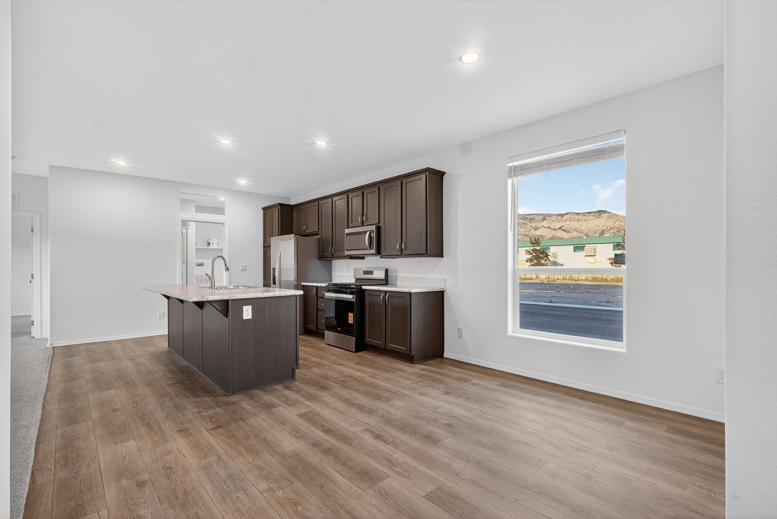 Kitchen with dark brown cabinets, an island with sink, stainless steel appliances, a kitchen bar, and light wood-style flooring