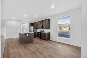 Kitchen with dark brown cabinets, an island with sink, stainless steel appliances, a kitchen bar, and light wood-style flooring