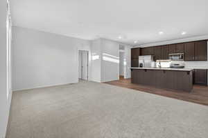 Kitchen featuring dark colored carpet, open floor plan, stainless steel appliances, a kitchen bar, and an island with sink