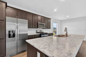 Kitchen featuring stainless steel appliances, dark brown cabinets, light wood-type flooring, a kitchen island with sink, and recessed lighting