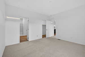 Unfurnished bedroom featuring a walk in closet, light colored carpet, and ensuite bath