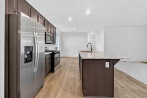 Kitchen featuring dark brown cabinets, appliances with stainless steel finishes, light wood-style floors, recessed lighting, and a kitchen island with sink